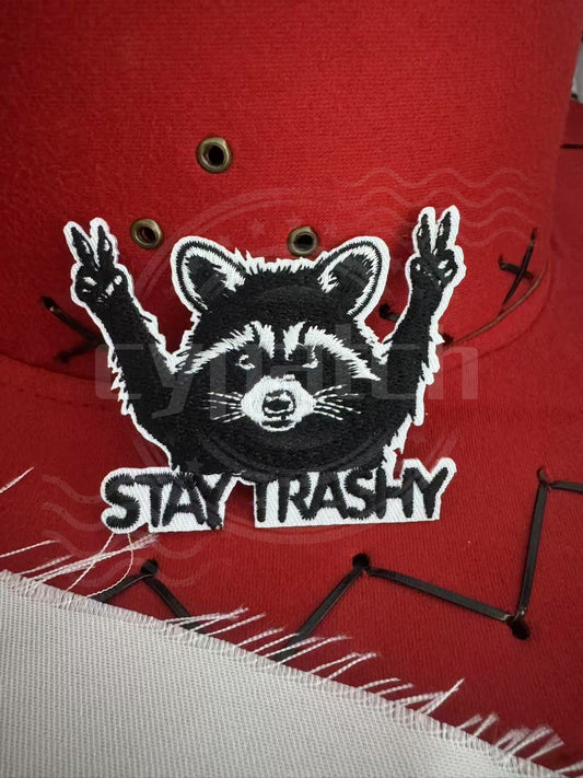 Embroidered raccoon patch saying 'Stay Trashy' with peace signs on red cap